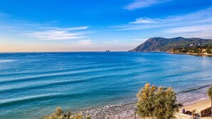 A coastal view with clear blue sea, a beach, and distant mountains.