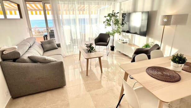 A modern living room with a grey sofa, a coffee table, a TV, and a dining area with chairs and a table.