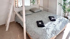 A bunk bed with a ladder, a mirror with lights, a patterned bedspread, and a potted plant.