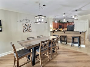 Een ruime eethoek met een houten tafel en stoelen, een keuken op de achtergrond, en hanglampen.
