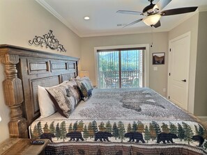A bedroom with a large bed, a ceiling fan, a view of the outdoors through a sliding glass door, and a decorative wall piece. - Legacy at the Summit - 2 Balconies, Mountain Views, Walk Downtown (Gatlinburg)