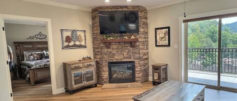 A living room with a stone fireplace, a flat-screen TV mounted above it, and a ceiling fan.