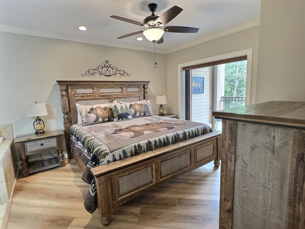 A bedroom with a wooden bed, two bedside tables with lamps, a ceiling fan, and a window with a view of trees. - UPDATED Luxury condo in Downtown Gatlinburg. Walk to everything!  (Gatlinburg)