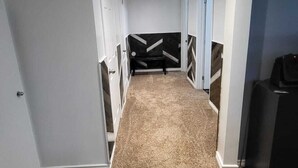 A hallway with carpeted floors, white walls, and a black bench in the center. - Spacious and Modern Home, 10 mins to Restaurants, Shops and Parks. (Welland)
