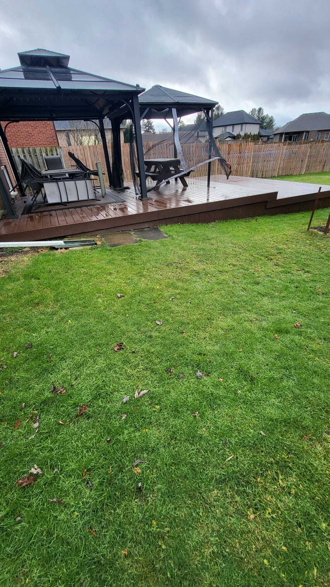 Un jardin avec une terrasse en bois, un patio couvert et une pelouse.