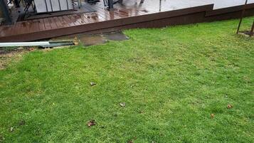 Un jardin avec une terrasse en bois, un patio couvert et une pelouse.