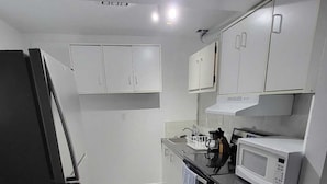 A compact kitchen with white cabinets, a black refrigerator, a microwave, and a stove. - Spacious and Modern Home, 10 mins to Restaurants, Shops and Parks. (Welland)