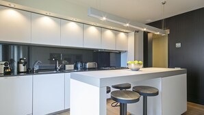 A modern kitchen with white cabinetry, a black countertop, and a central island with stools. - Paseo de Gracia1 (Barcelona)