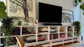 A modern living room with a flat-screen TV, a bookshelf filled with books, a framed artwork, and a woven rug. - Cozy & Modern Victorian in Historic Allentown, Buffalo (Buffalo)