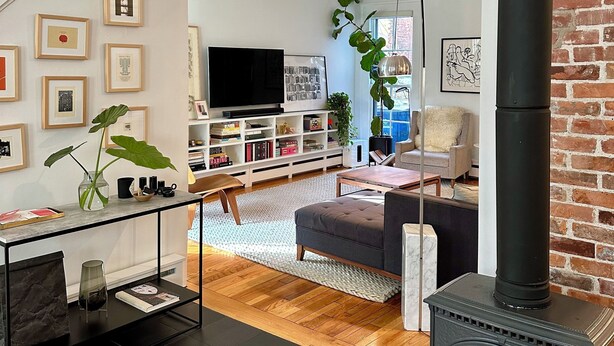 A modern living room with a wooden floor, a black fireplace, a staircase, and a bookshelf with framed pictures. - Cozy & Modern Victorian in Historic Allentown, Buffalo (Buffalo)