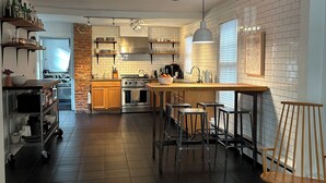 A modern kitchen with a central island, wooden flooring, and a brick accent wall. - Cozy & Modern Victorian in Historic Allentown, Buffalo (Buffalo)