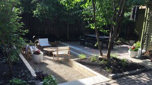 A backyard patio with a wooden table and chairs, surrounded by potted plants and a small garden bed. - Cozy & Modern Victorian in Historic Allentown, Buffalo (Buffalo)