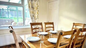A dining table set for four with wooden chairs, a window with curtains, and a view of a garden. - Cosy Self Catering Family Home in a Quaint Village Setting (Wetherby)