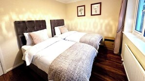 A hotel room with two beds, a window with curtains, and a radiator. - Cosy Self Catering Family Home in a Quaint Village Setting (Wetherby)