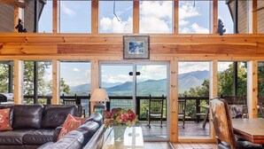 Ein gemütliches Interieur mit einem Ledersofa, einem Couchtisch mit Blumen und Bergblick durch große Fenster.