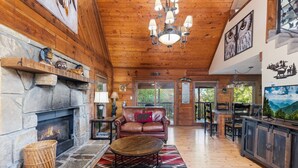A cozy lodge interior with a stone fireplace, leather furniture, and wooden beams. - Cherokee Winds - 2bd 3bth in Chalet Village w/ Mountain Vews! (Gatlinburg)