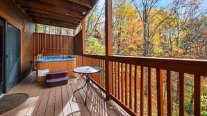 A wooden deck with a hot tub, a table, and a view of autumn trees. - Cherokee Winds - 2bd 3bth in Chalet Village w/ Mountain Vews! (Gatlinburg)