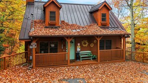 A wooden cabin with a sloped roof, a porch with a bench, and a sign indicating it is a heritage site. - Cherokee Winds - 2bd 3bth in Chalet Village w/ Mountain Vews! (Gatlinburg)