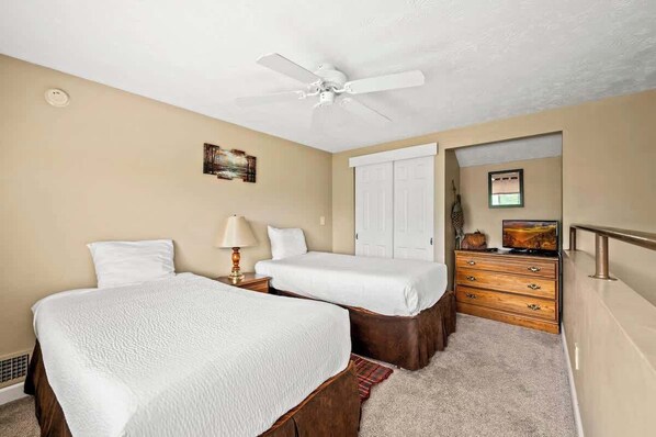 A bedroom with two beds, a ceiling fan, a dresser, and a television.