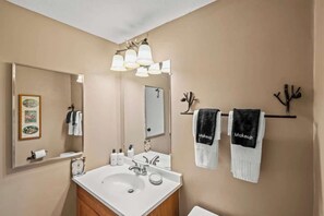 Ein Badezimmer mit einem weißen Waschbecken, Spiegel und Handtuchhalter mit zwei Handtüchern, eines beschriftet mit 'Makeup'.