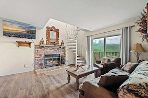 Ein Wohnzimmer mit Kamin, einem großen Spiegel, einer Treppe und Blick ins Freie.