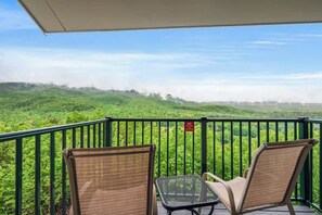 Ein Balkon mit zwei Korbstühlen mit Blick auf eine üppige, grüne Landschaft.