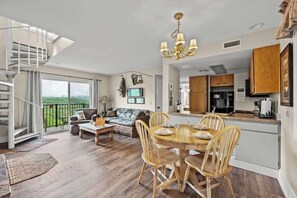 A spacious living room with a dining area, a staircase, and a view of the outdoors.