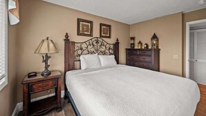 Een slaapkamer met een groot bed, een nachtkastje met lamp, een dressoir en twee ingelijste foto's aan de muur.