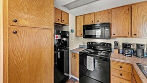 A compact kitchen with wooden cabinets, a black stove, a microwave, and a coffee maker. - Smoky Mountain Condo w/ Heated Pool & Sauna Access (Gatlinburg)