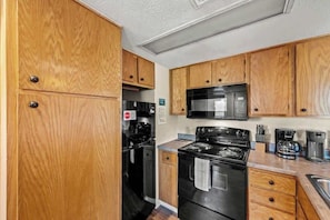 A compact kitchen with wooden cabinets, a black stove, a microwave, and a coffee maker. - Smoky Mountain Condo w/ Heated Pool & Sauna Access (Gatlinburg)