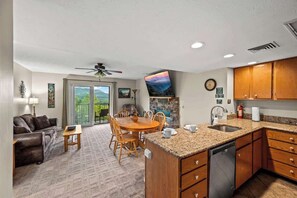 A spacious living area with a dining table, a kitchen with wooden cabinets, and a large window offering a view of the outdoors.