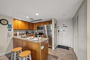 A compact kitchen with wooden cabinets, stainless steel appliances, and a small island with stools.