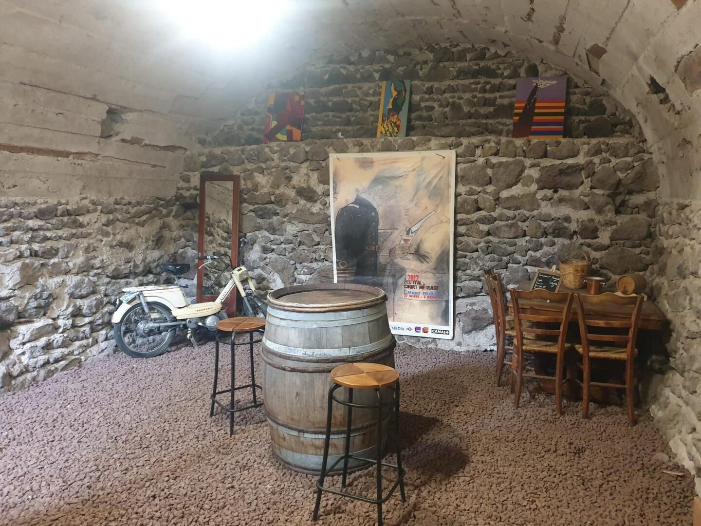 Una habitación rústica con paredes de piedra, una motocicleta antigua, barriles de madera y un cartel en la pared.