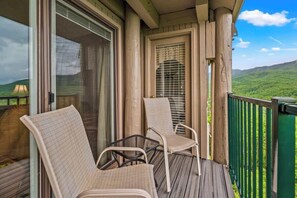 Un balcon avec des fauteuils en osier et une vue sur un paysage verdoyant.