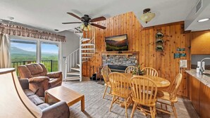 Una sala de estar acogedora con chimenea, paredes de madera, comedor y balcón con vistas panorámicas.
