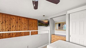 Ein Schlafzimmer mit geneigter Decke, einem an der Wand montierten Fernseher, einer Holzvertäfelung, einer weißen Tür und einem Bett.