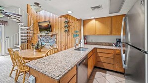 Una cocina con armarios de madera, encimeras de granito, refrigerador de acero inoxidable y lavavajillas integrado.