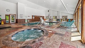 Ein großer Innenpoolbereich mit Whirlpool, Liegestühlen und einer Holzverkleidung.