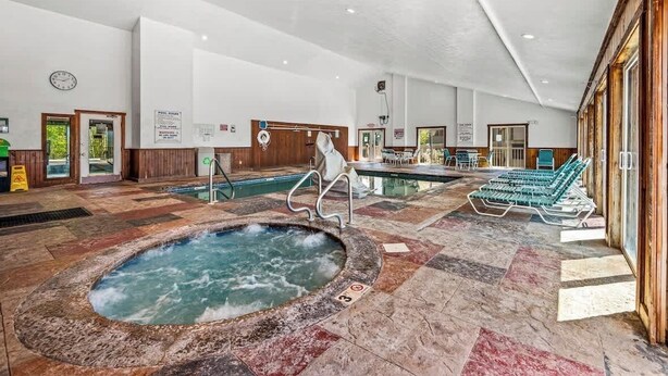 Amplia zona de piscina interior con jacuzzi, sillas de descanso y una pared de madera.
