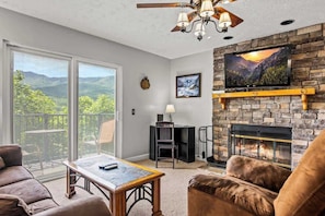 Ein Wohnzimmer mit Kamin, einem an einer Steinwand befestigten Fernseher und einem Balkon mit Bergblick.