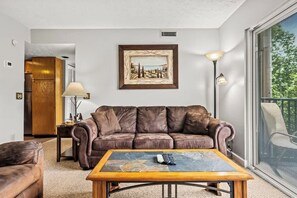 A living room with a brown leather sofa, a coffee table with a remote control, a framed picture on the wall, and a lamp.
