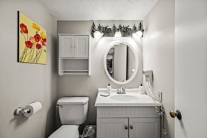 Ein Badezimmer mit Toilette, Waschbecken mit Spiegel, Schrank und Toilettenpapierhalter.