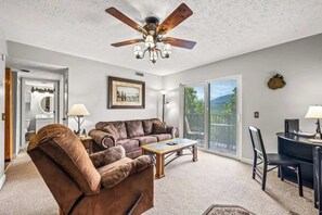 A living room with a ceiling fan, a brown leather sofa, a wooden coffee table, and a desk with a chair.