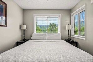 A bedroom with a large bed, two bedside tables, and a window with blinds.