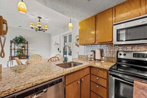 A kitchen with granite countertops, wooden cabinets, a stainless steel sink, a built-in oven, and a chandelier.