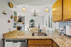A kitchen with granite countertops, stainless steel appliances, wooden cabinets, and pendant lighting.