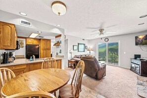Amplia sala de estar con una mesa de comedor, armarios de madera y un gran ventanal con vistas a un balcón.
