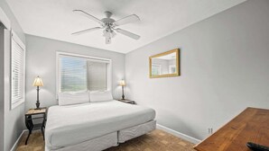 Un dormitorio con una cama, dos lámparas de noche, un ventilador de techo, una mesita de noche de madera, un aparador de madera y un espejo en la pared.