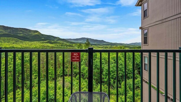 Un balcón con vistas a colinas verdes y montañas, un letrero que dice “NO SE PERMITE ASAR NI FUMAR”, y una silla de metal.