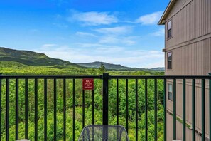 A balcony with a view of lush green hills and mountains, a "NO GRILLING OR SMOKING" sign, and a metal chair. - Mountain Views Indoor Pool Hot Tub Sleeps 4 (Gatlinburg)